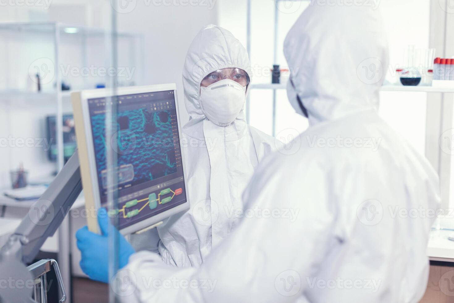 compañeros de trabajo en bata que se discute acerca de virus evolución vestido en ppe traje en moderno cuidado de la salud instalación. doctores examinando virus evolución utilizando alto tecnología investigando diagnóstico en contra covid19 foto