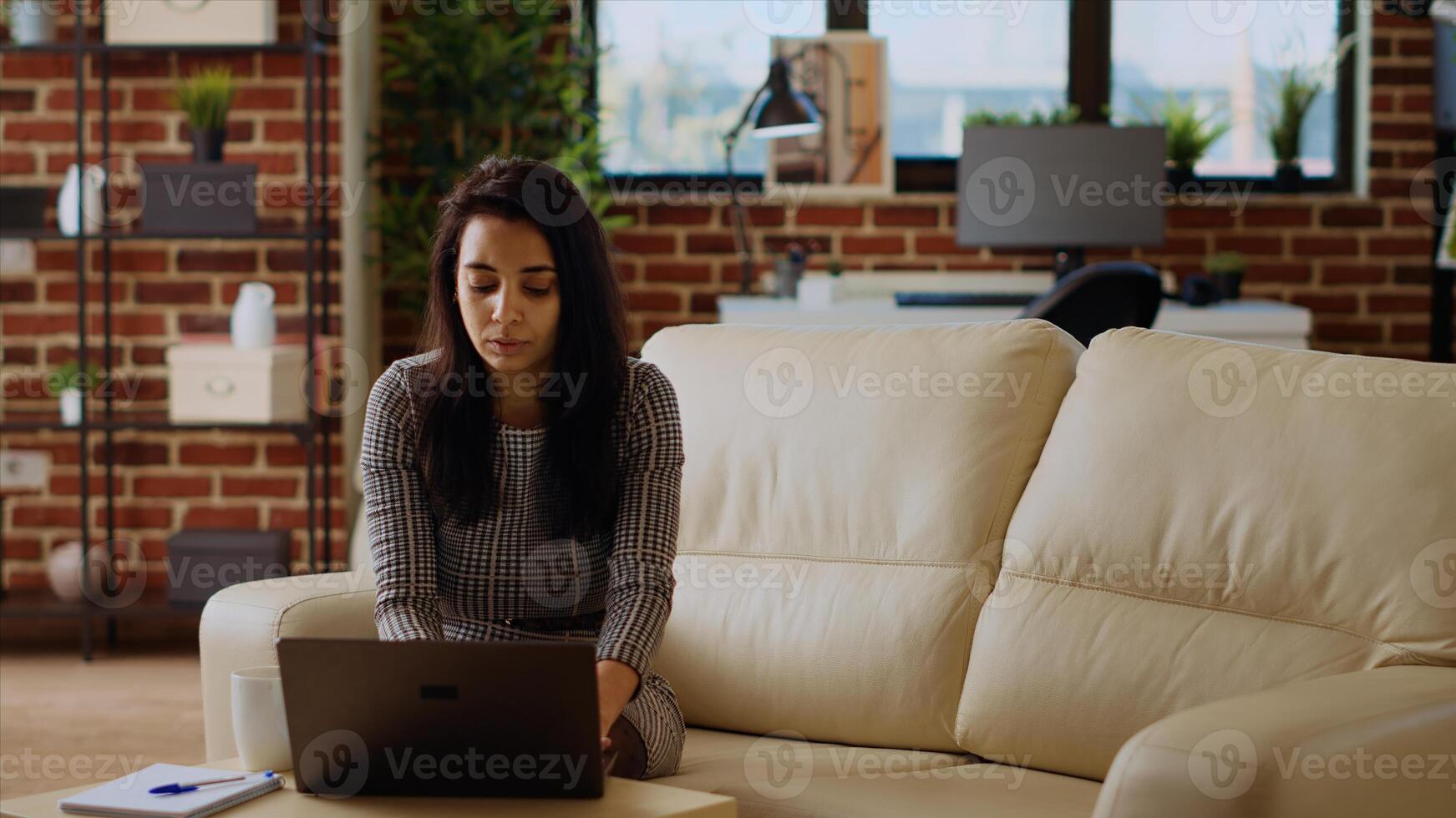 Indian teleworker sitting on couch, focused on finishing tasks in personal office. Remote worker concentrating on correctly inputting data on laptop, hurrying to complete project before deadline photo