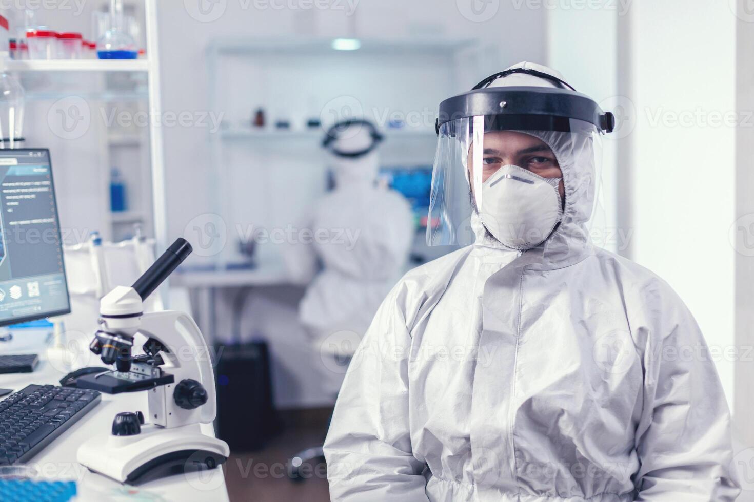 agotado médico sentado a lugar de trabajo vistiendo ppe traje con visera durante covid19 brote. sobrecargado de trabajo investigador vestido en protector traje en contra invección con coronavirus durante global epidemia. foto