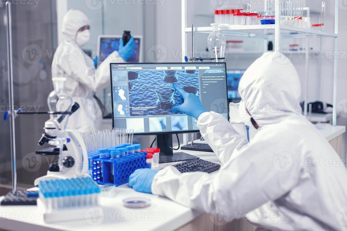 Healthcare doctors investigating evolution of coronavirus working on computer dressed in coverall. Lab engineers conducting experiment for vaccine development against covid19 virus photo