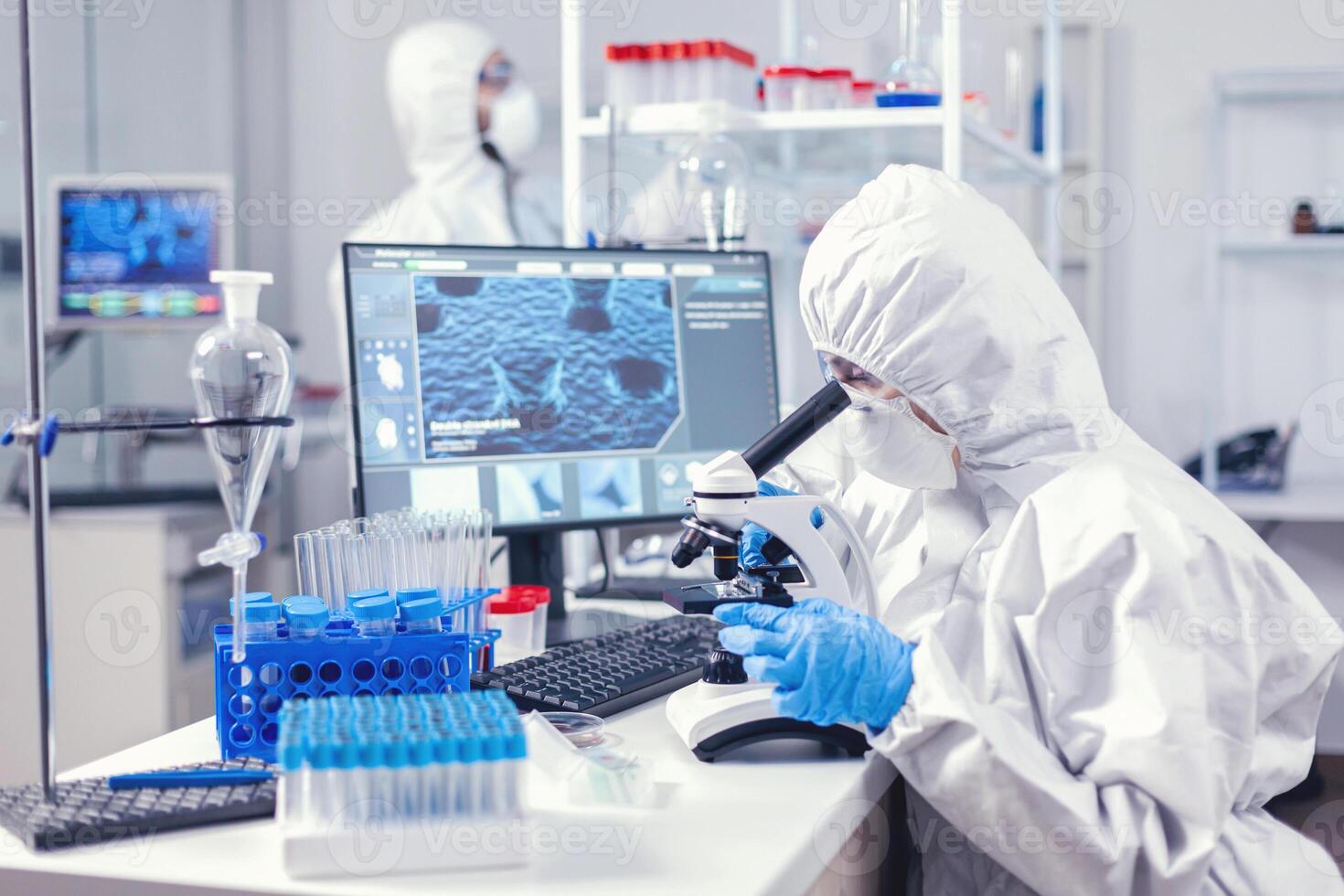 Team of medical personal wearing ppe suit doing coronavirus analysis in modern laboratory. Chemist researcher during global pandemic with covid-19 checking sample in biochemistry lab photo