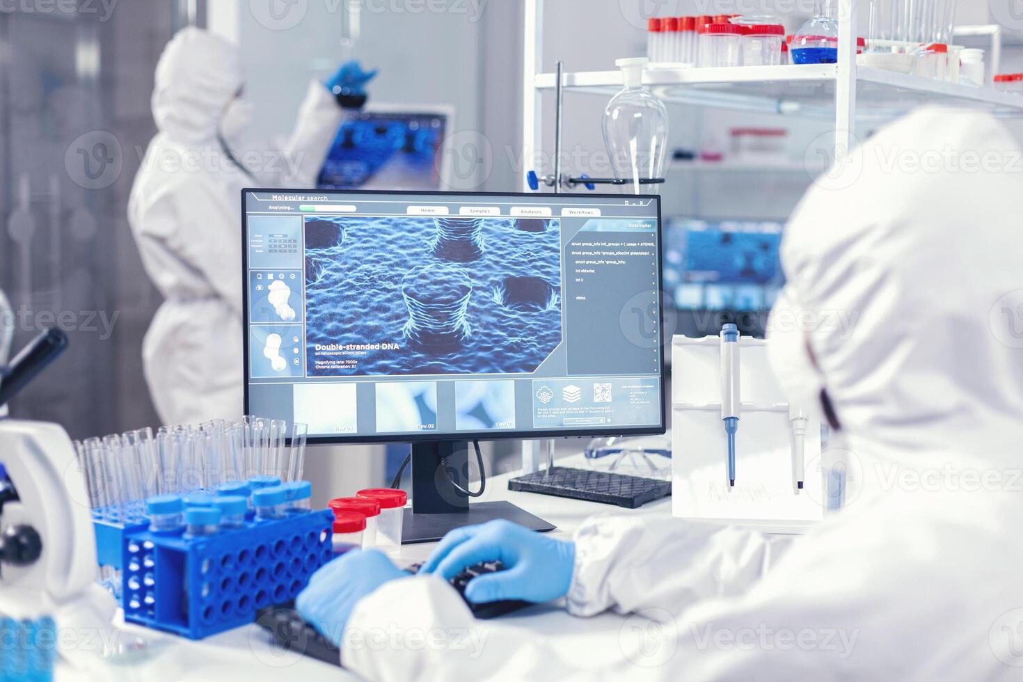 Scientist in modern lab working on computer during coronavirus dressed in ppe. Lab engineers conducting experiment for vaccine development against covid19 virus photo