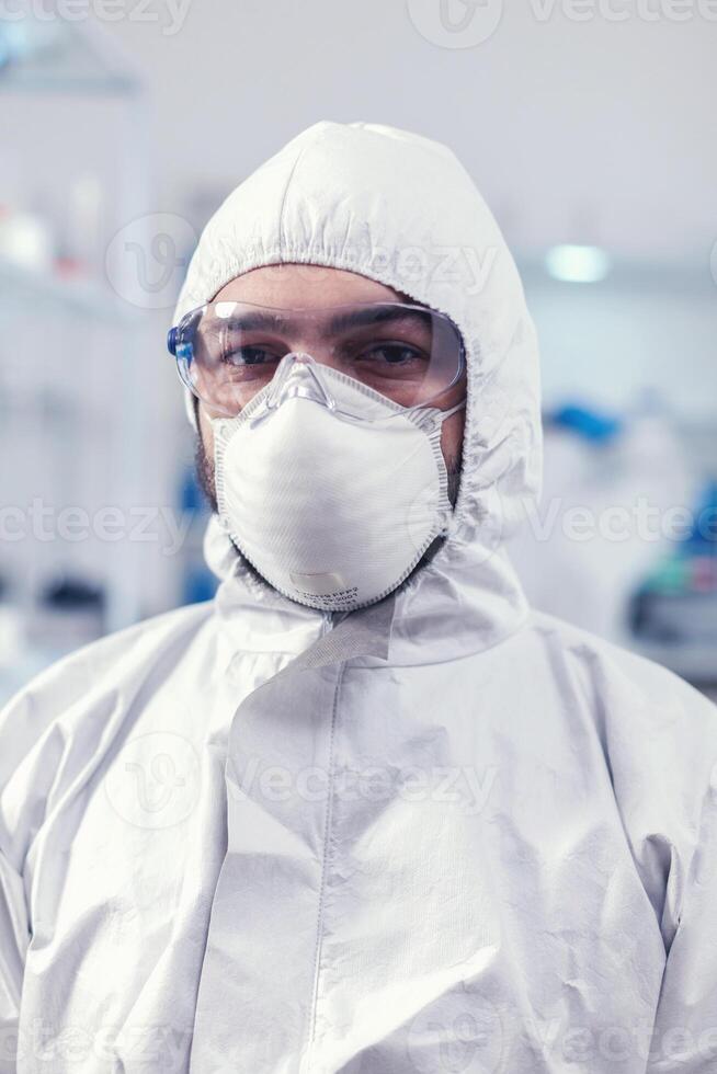 Close up of medicine engineer wearing face mask and suit in laboratory during covid019. Overworked researcher dressed in protective suit against invection with coronavirus during global epidemic. photo