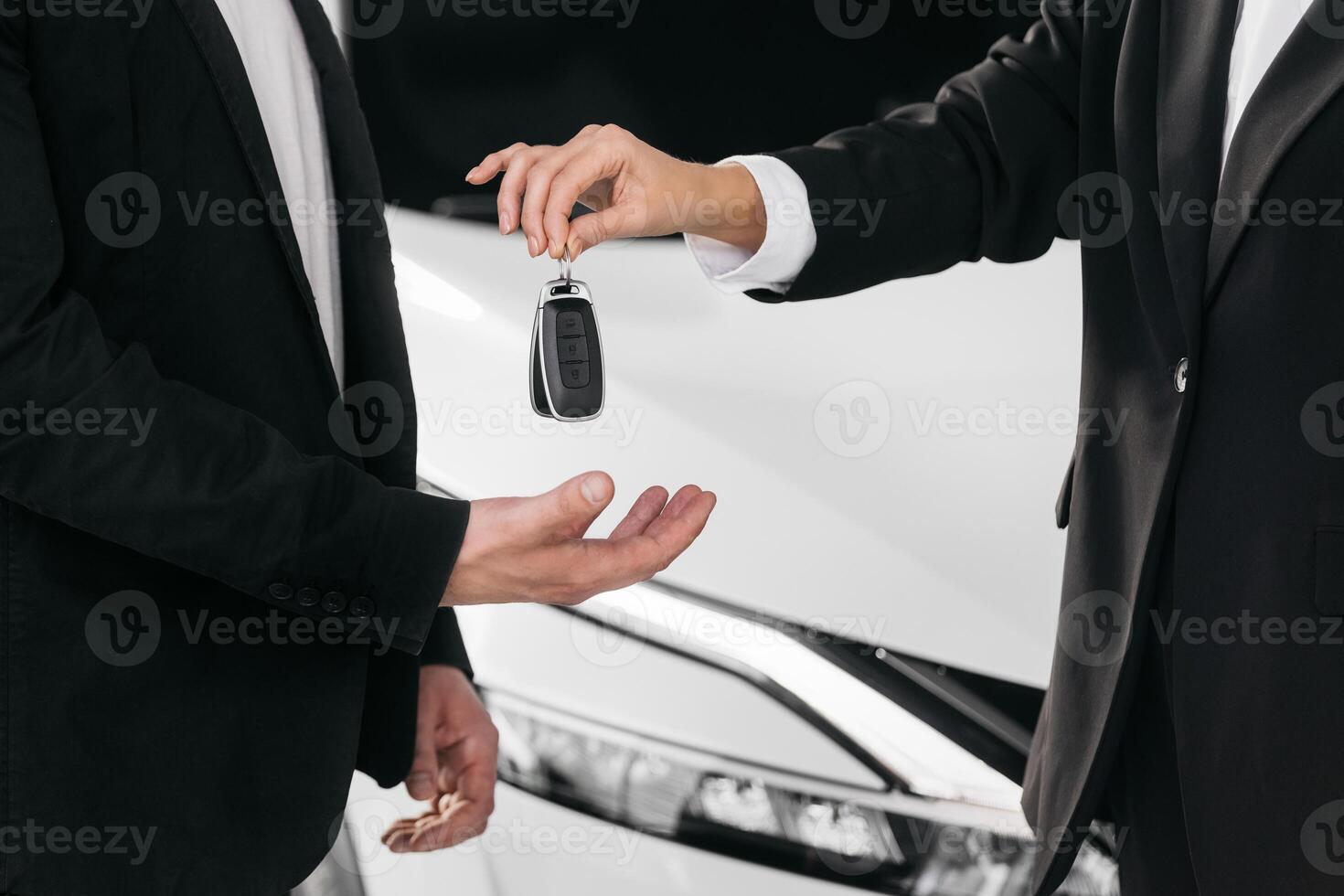 Male hand gives a car keys to female hand in the car dealership close up. Unrecognized auto seller and a man who bought a vehicle shake hands. Dealer giving key to new owner in auto show or salon photo