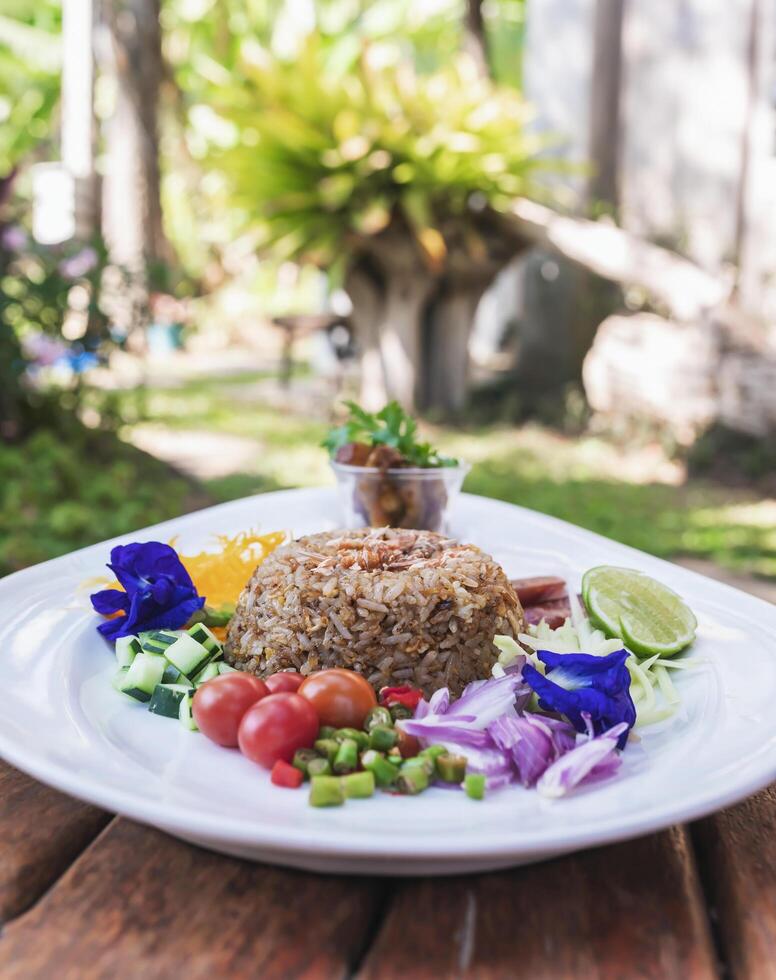 Thai food, shrimp paste fried rice consists of cucumber, tomato, sliced hot peppers, shallots, sliced raw mango, lime, topped with seasoning sauce. photo