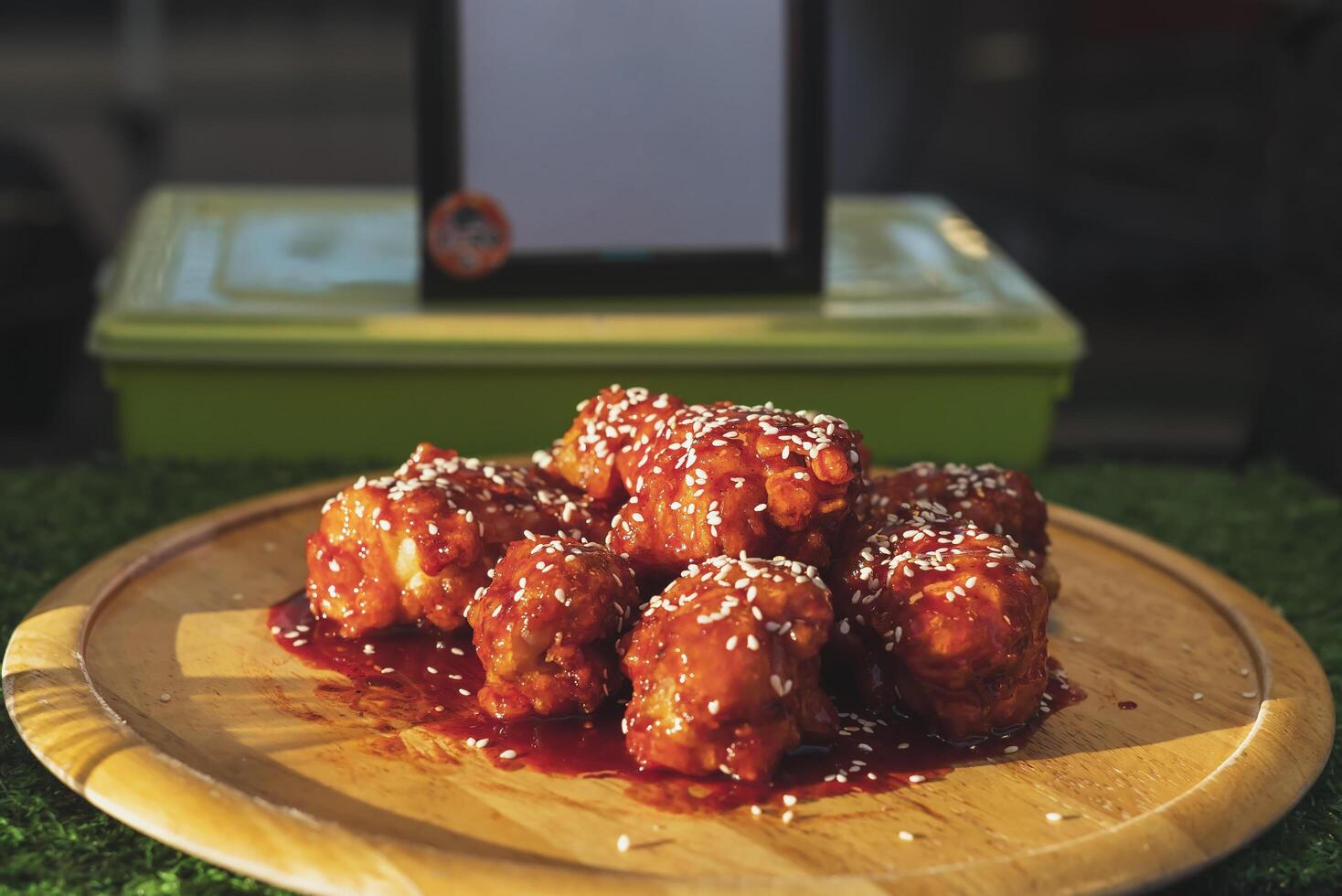 Small pieces of chicken topped with tomato sauce and white sesame seeds are placed on a wooden plate. photo