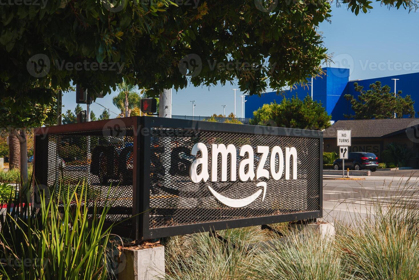 Security fence at Amazon facility with logo, trees, and blue building photo