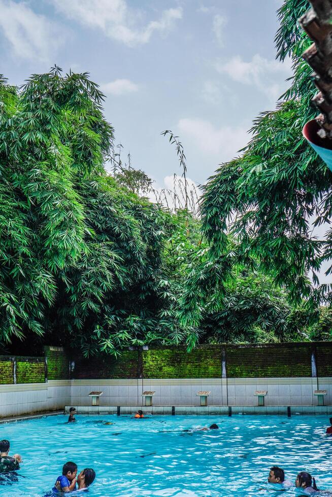 Jepara, Central Java, April 14, 2024 - Swimming pool rides surrounded by trees are full of visitors during holidays. photo