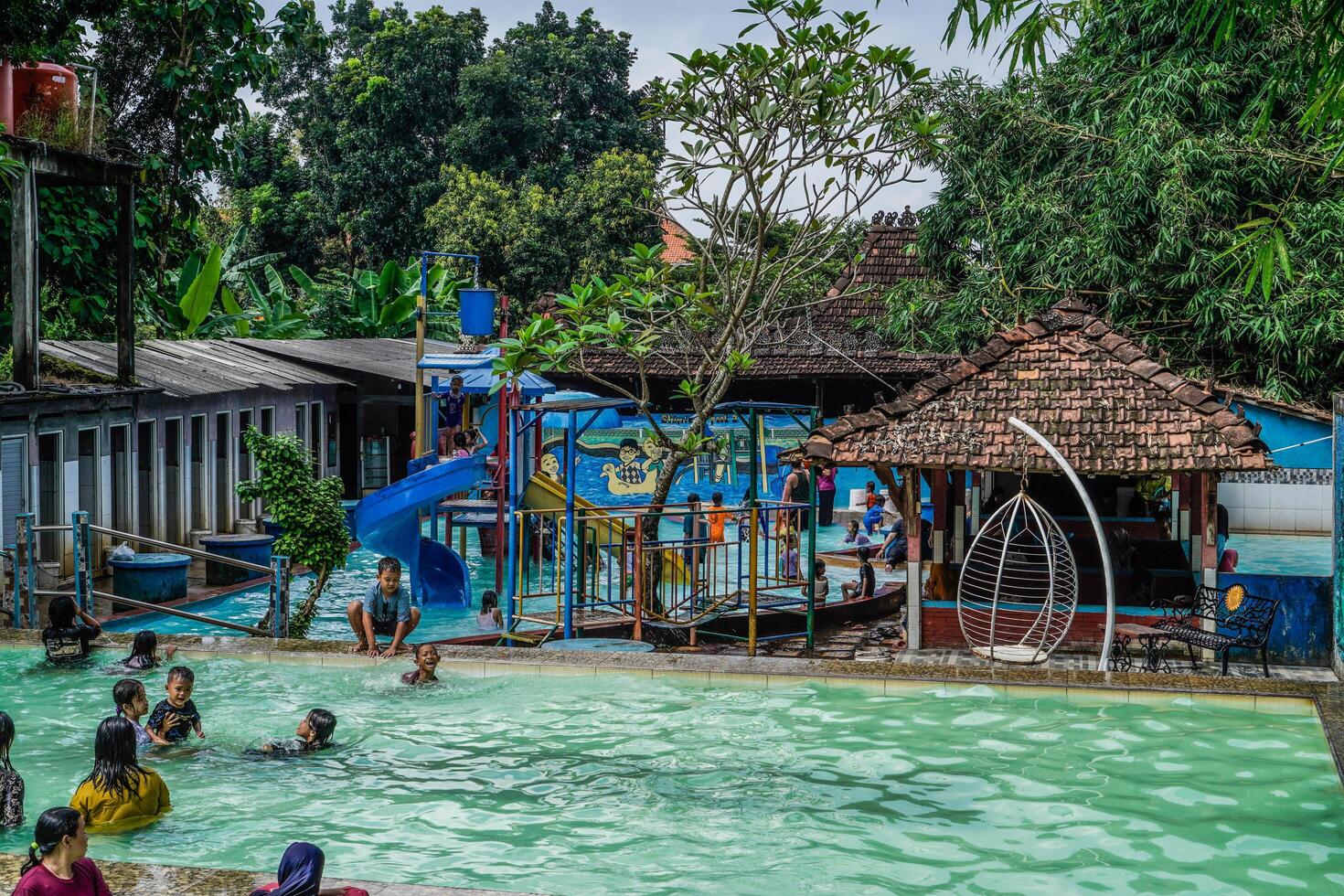 Jepara, Central Java, April 14, 2024 - Swimming pool rides surrounded by trees are full of visitors during holidays. photo