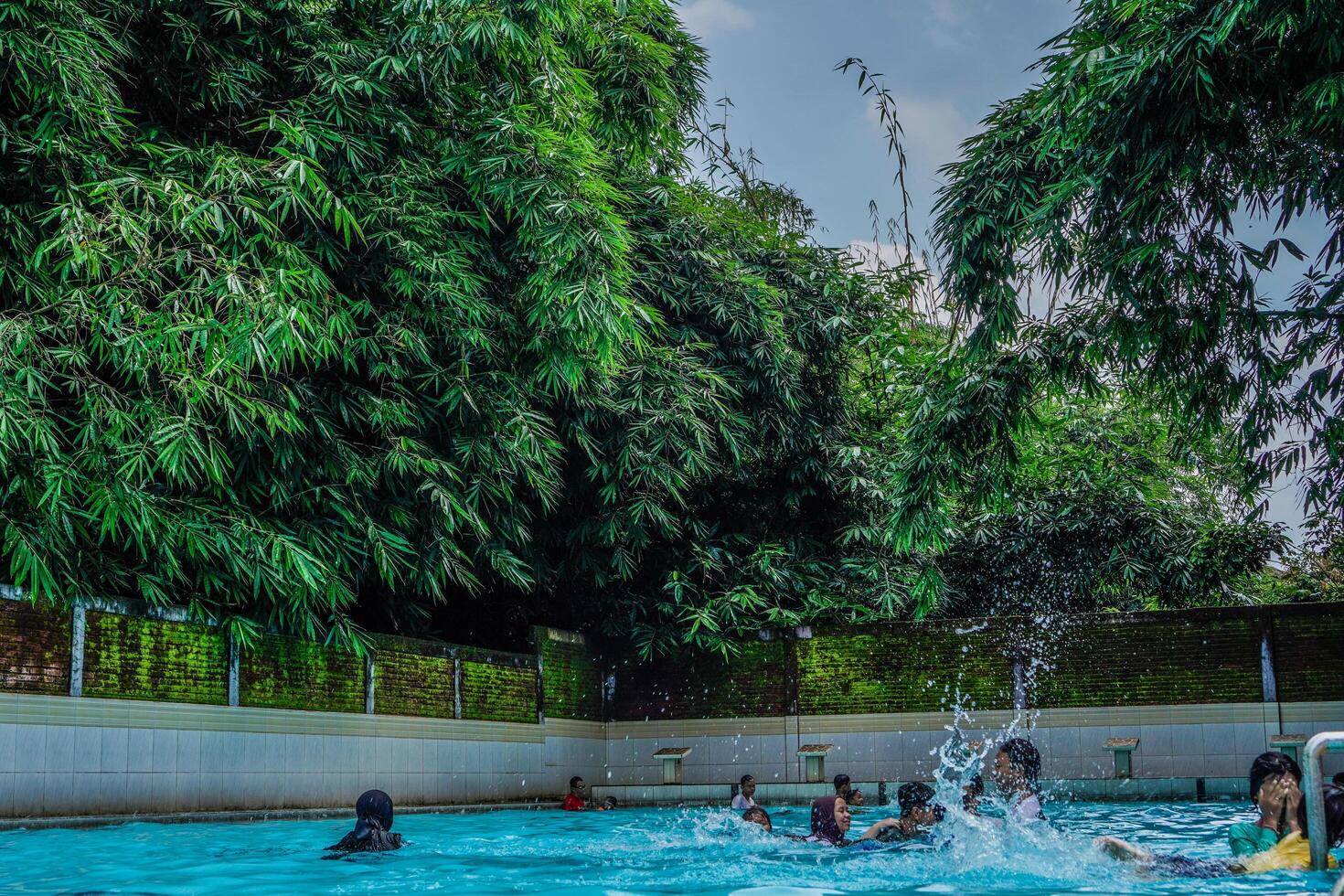 Jepara, Central Java, April 14, 2024 - Swimming pool rides surrounded by trees are full of visitors during holidays. photo
