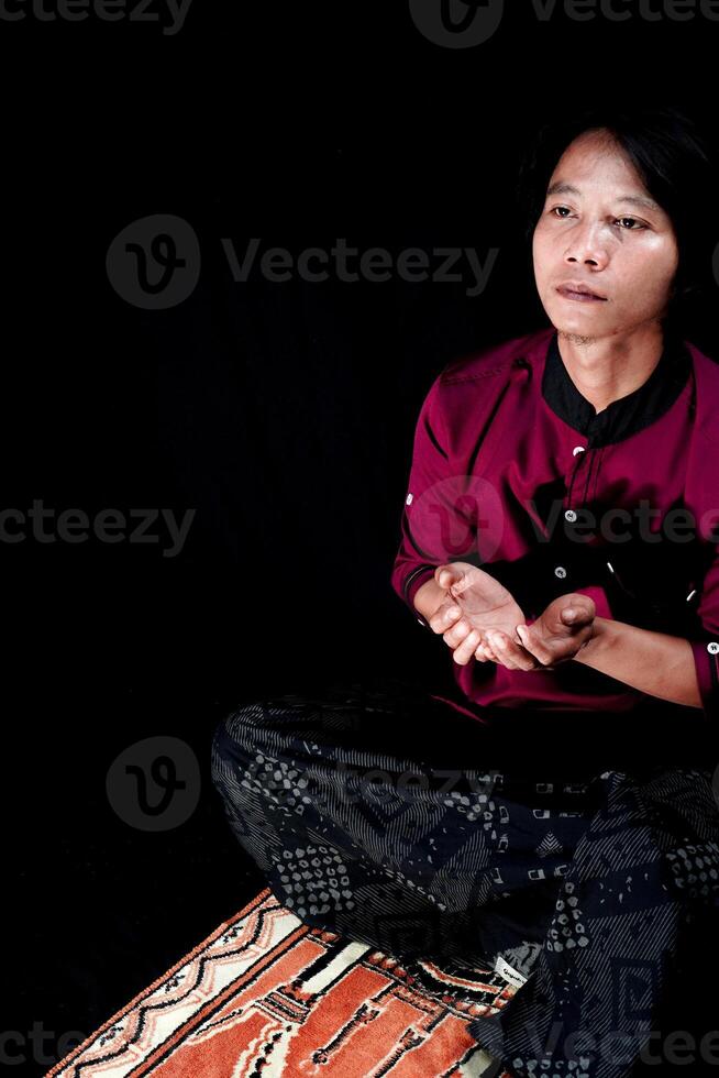 front view of a man praying on a prayer mat with a black background. photo