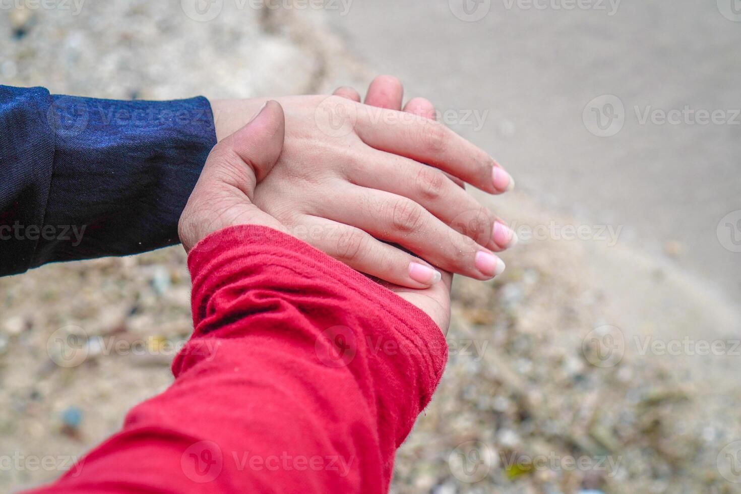 the hands of a couple holding hands against the background of beach sand. photo