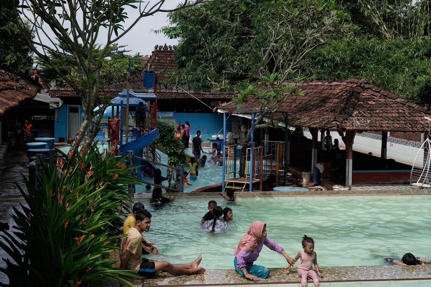 Jepara, Central Java, April 14, 2024 - Swimming pool rides surrounded by trees are full of visitors during holidays. photo
