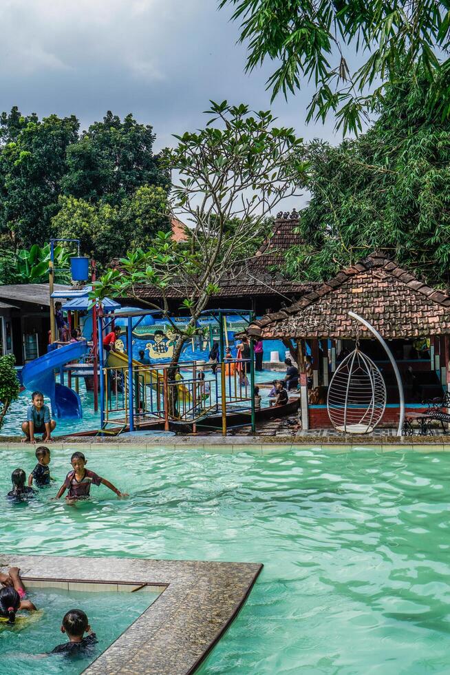 Jepara, Central Java, April 14, 2024 - Swimming pool rides surrounded by trees are full of visitors during holidays. photo