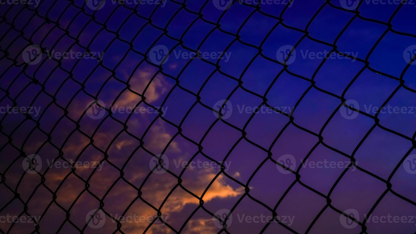 shot of the iron net fence against the background of an orange sky in the afternoon. photo