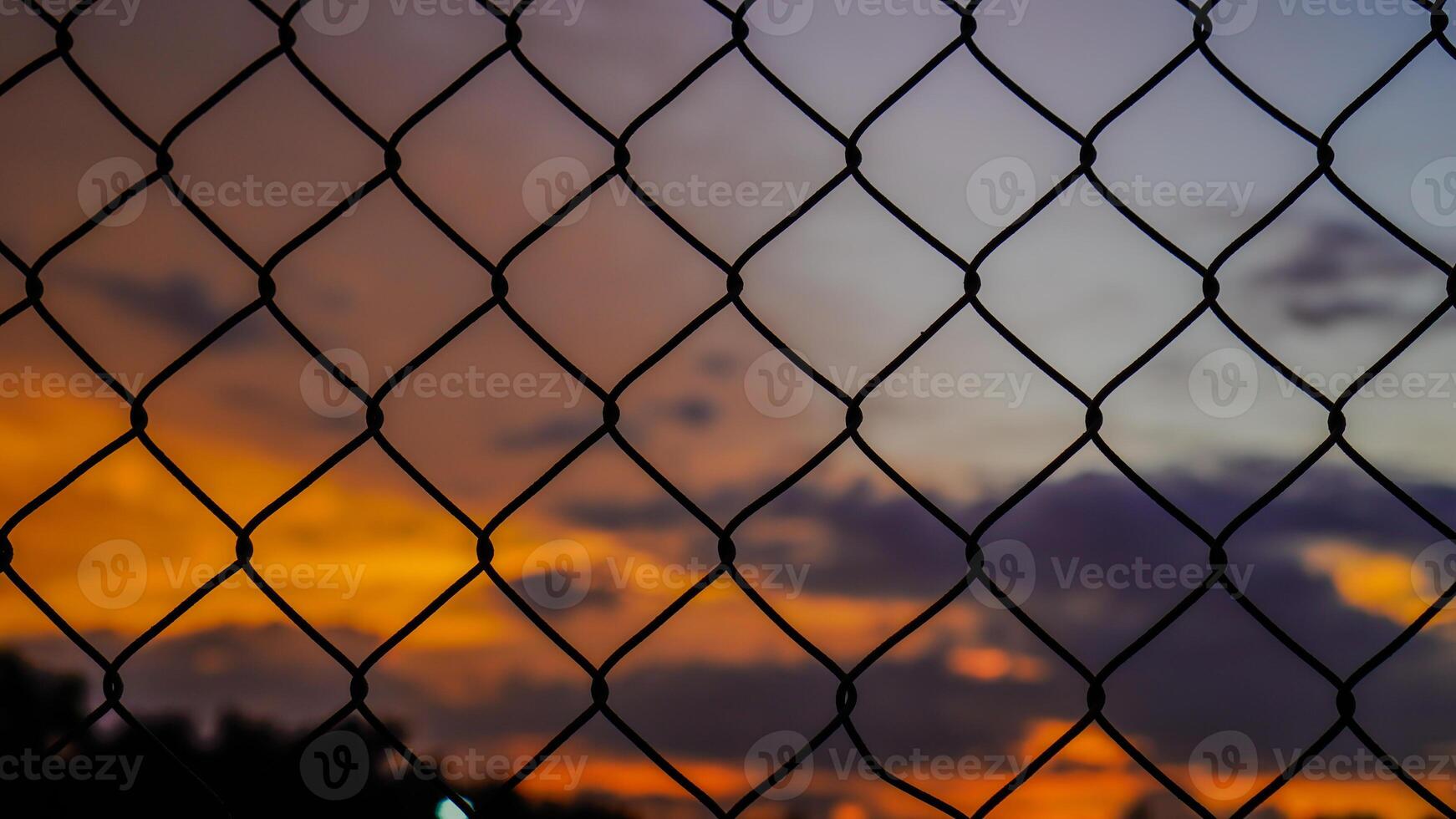 shot of the iron net fence against the background of an orange sky in the afternoon. photo