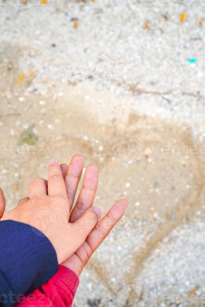 the hands of a couple holding hands against the background of beach sand. photo