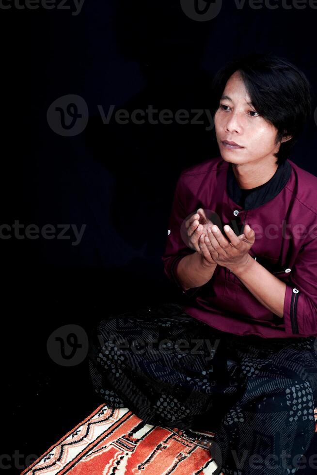 front view of a man praying on a prayer mat with a black background. photo