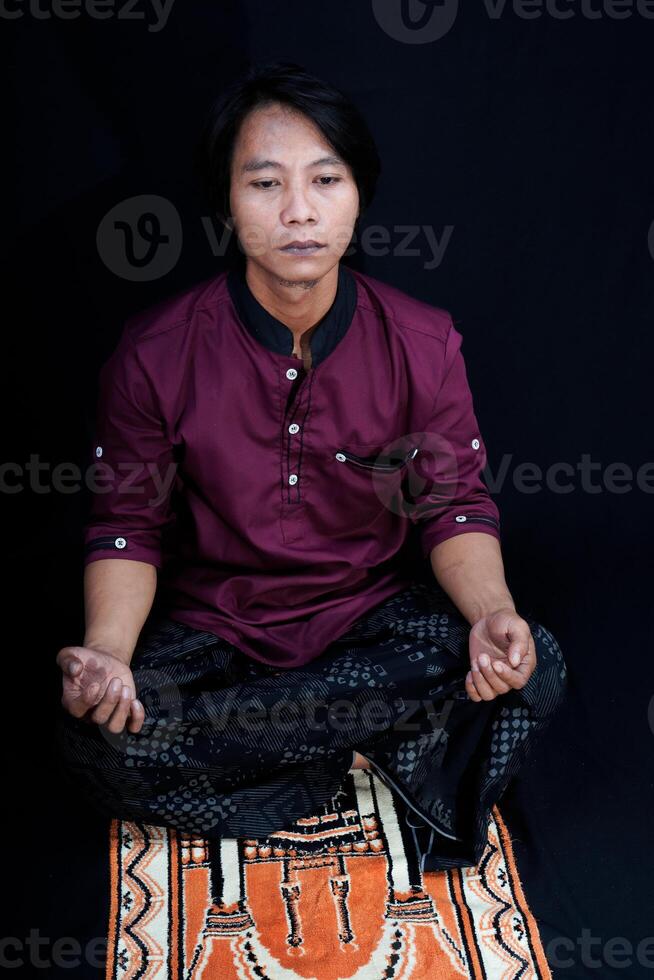 front view of a man praying on a prayer mat with a black background. photo