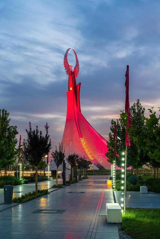 UZBEKISTAN, TASHKENT - SEPTEMBER 15, 2023 Illuminated monument of independence in the form of a stele with a Humo bird in the New Uzbekistan park at nighttime in autumn. photo