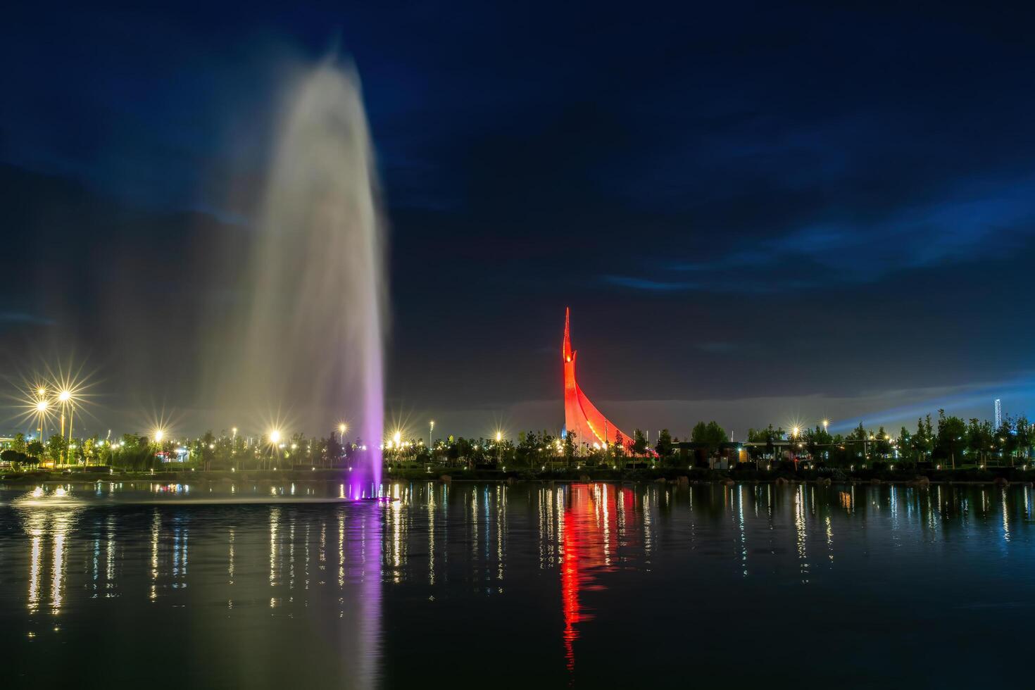 UZBEKISTAN, TASHKENT - SEPTEMBER 15, 2023 Illuminated monument of independence in the form of a stele with a Humo bird and fountain in the New Uzbekistan park at nighttime in autumn. photo