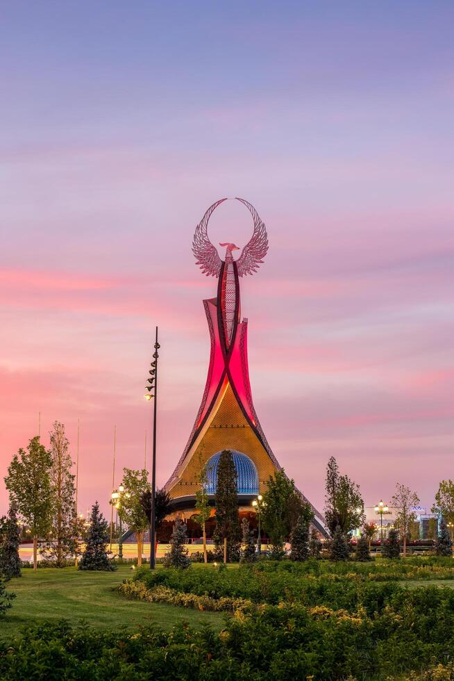 UZBEKISTAN, TASHKENT - SEPTEMBER 15, 2023 Monument of Independence in the form of a stele with a Humo bird on a twilight with dramatic cliods in the New Uzbekistan park. photo