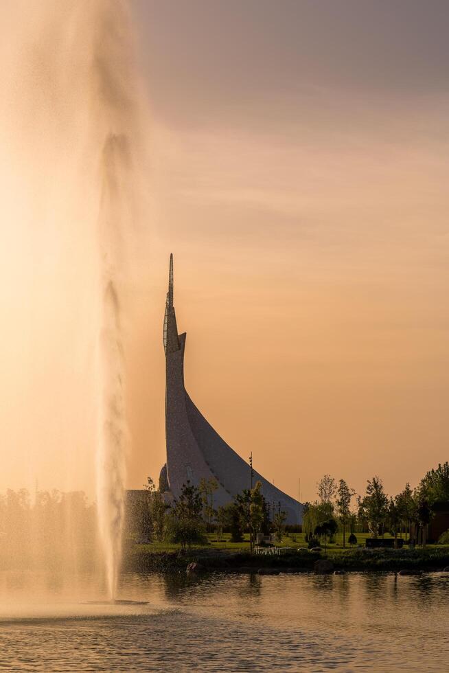 uzbekistán, Tashkent - septiembre 15, 2023 Monumento de independencia en el formar de un estela con un humo pájaro en un puesta de sol con dramático clidos en el nuevo Uzbekistán parque. foto