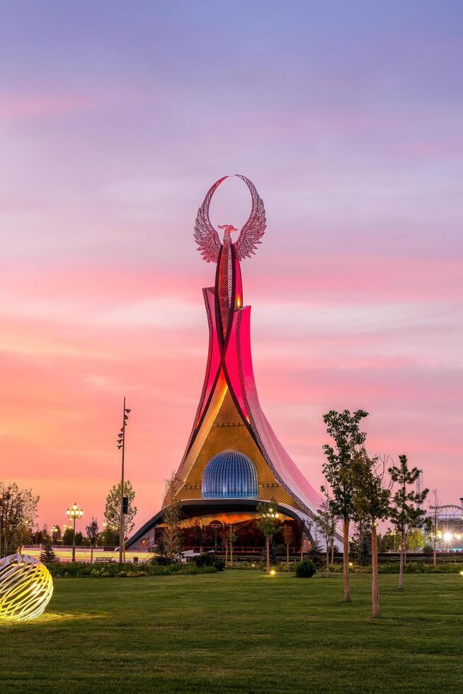 UZBEKISTAN, TASHKENT - SEPTEMBER 15, 2023 Monument of Independence in the form of a stele with a Humo bird on a twilight with dramatic cliods in the New Uzbekistan park. photo