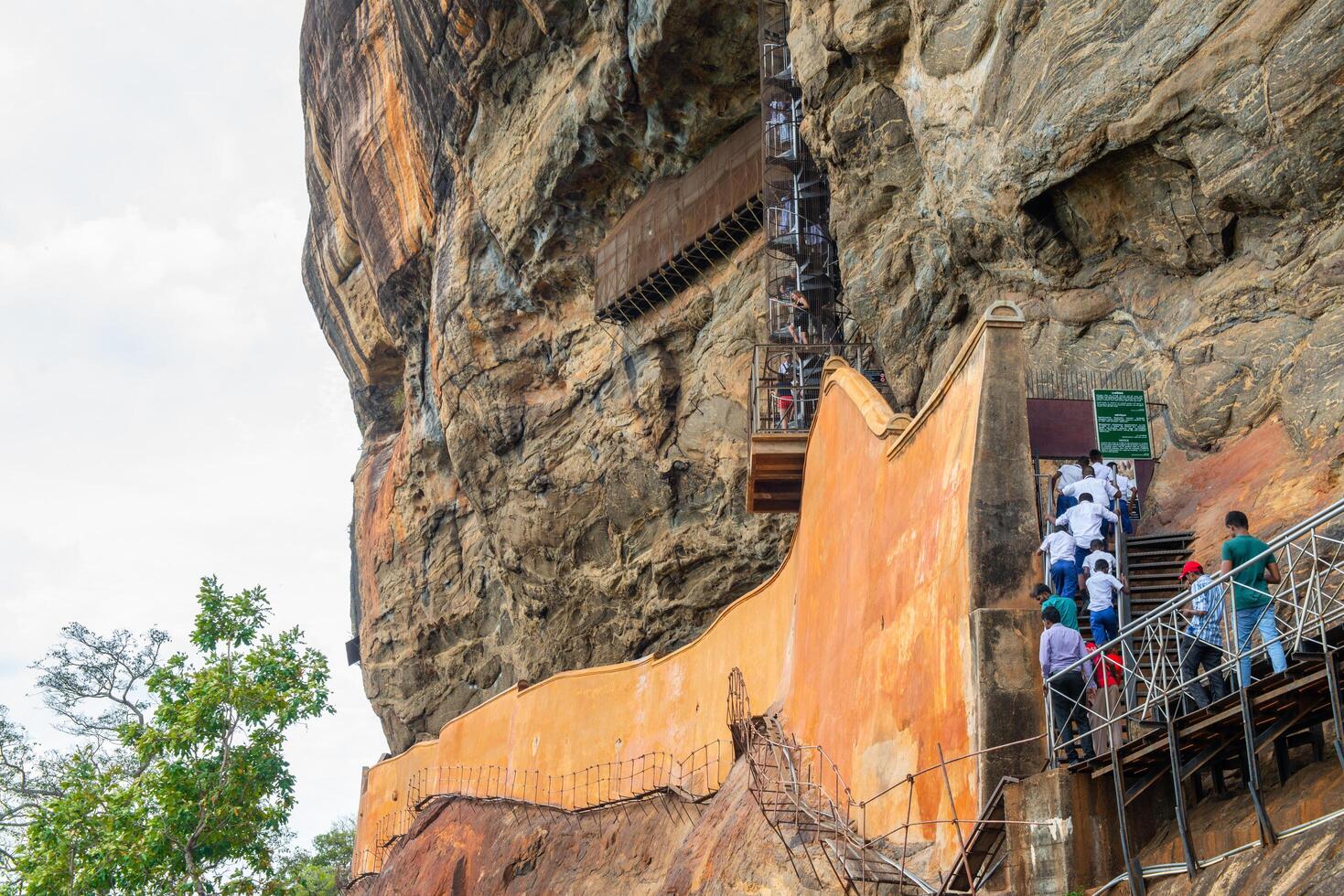 Sigiriya, Sri Lanka - August-07-2019 - Group of tourist climbing staircase to visit the Mirror wall in Sigiriya. In the old days it was polished so thoroughly that the king could see his reflection. photo