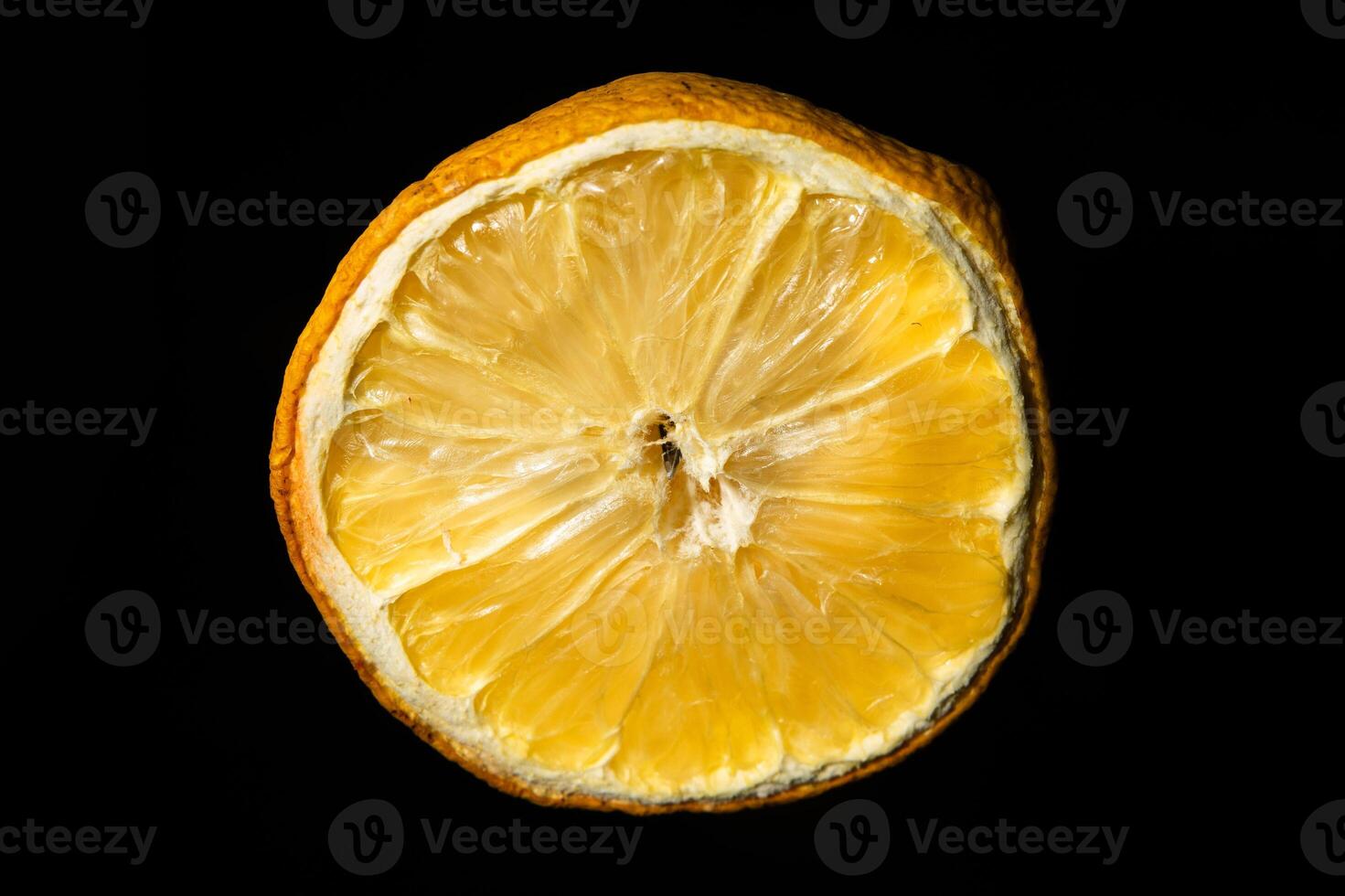 A cross-section of a dried lemon against a black background. The fading pulp and prominent membranes hint at aging, while the weathered texture adds depth to this close-up shot. photo