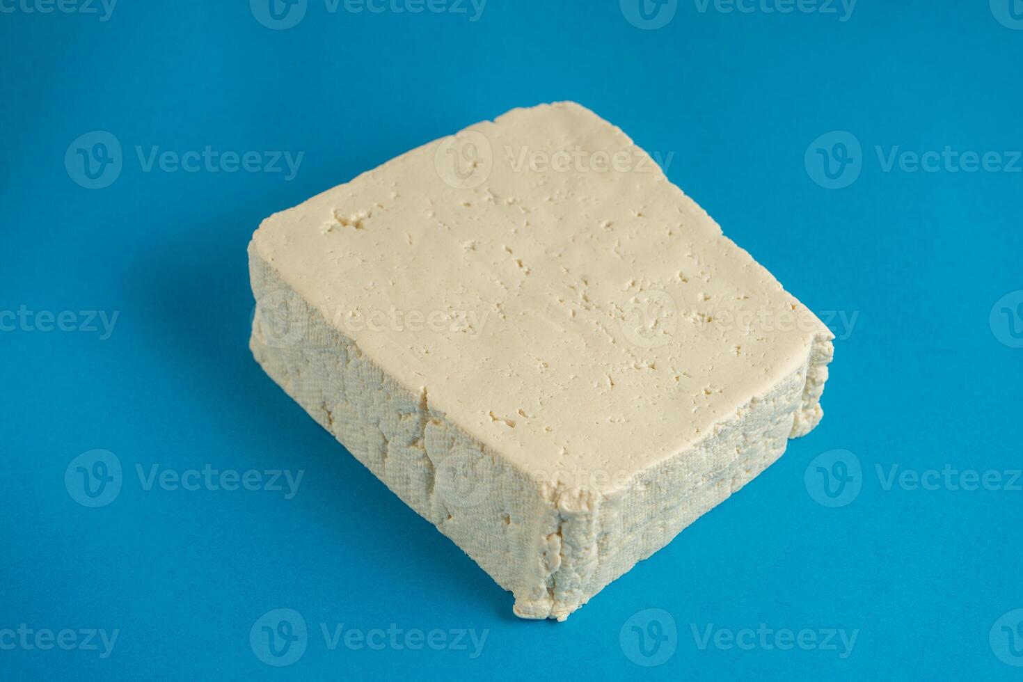 A block of white tofu sits against a bright blue background, its smooth texture and clean edges creating a simple yet striking contrast. Ideal for health and plant-based food themes. photo