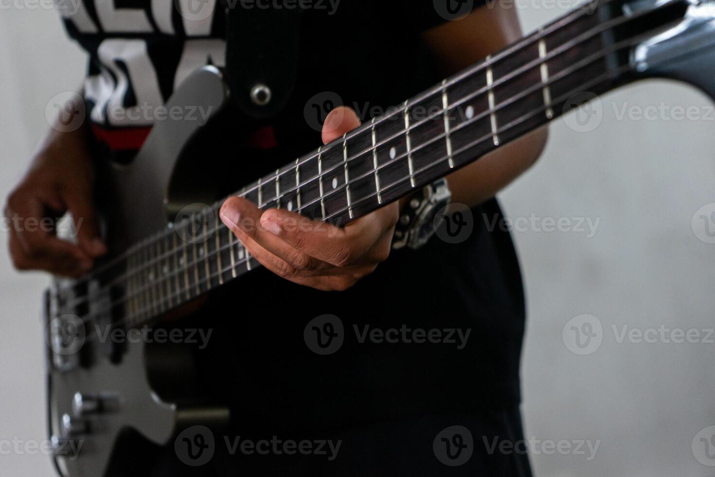 A man playing a bass guitar in a casual setting. He's focused on his instrument, fingers gliding over the strings. His relaxed posture and casual attire suggest a laid-back music session. photo