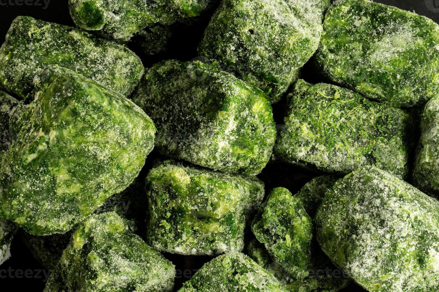 A cluster of frozen spinach leaves, covered in a thin layer of frost, lies neatly stacked. The vibrant green contrasts with the icy coating, highlighting the freshness preserved in each leaf. photo