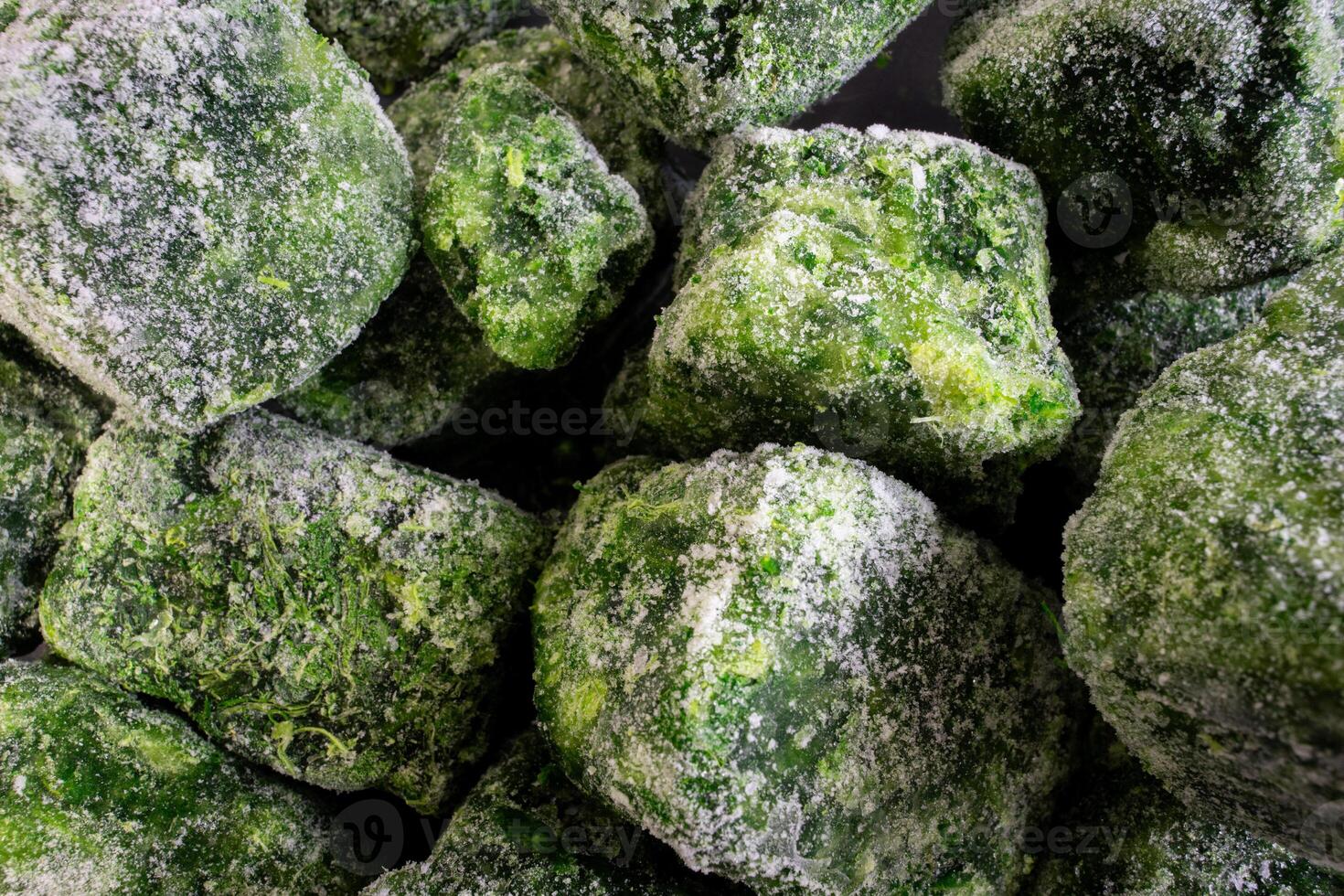 A cluster of frozen spinach leaves, covered in a thin layer of frost, lies neatly stacked. The vibrant green contrasts with the icy coating, highlighting the freshness preserved in each leaf. photo