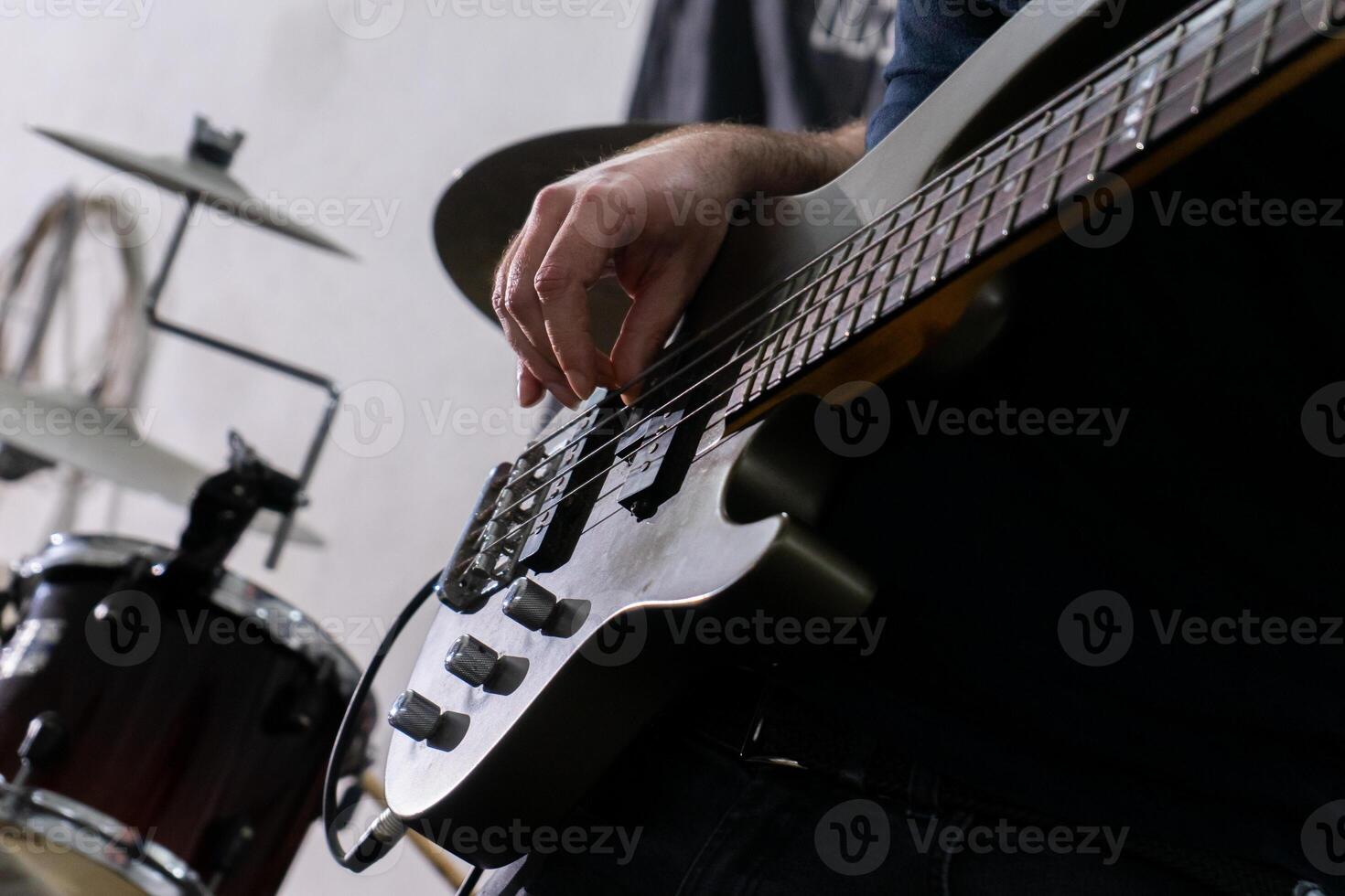 A man playing a bass guitar in a casual setting. He's focused on his instrument, fingers gliding over the strings. His relaxed posture and casual attire suggest a laid-back music session. photo