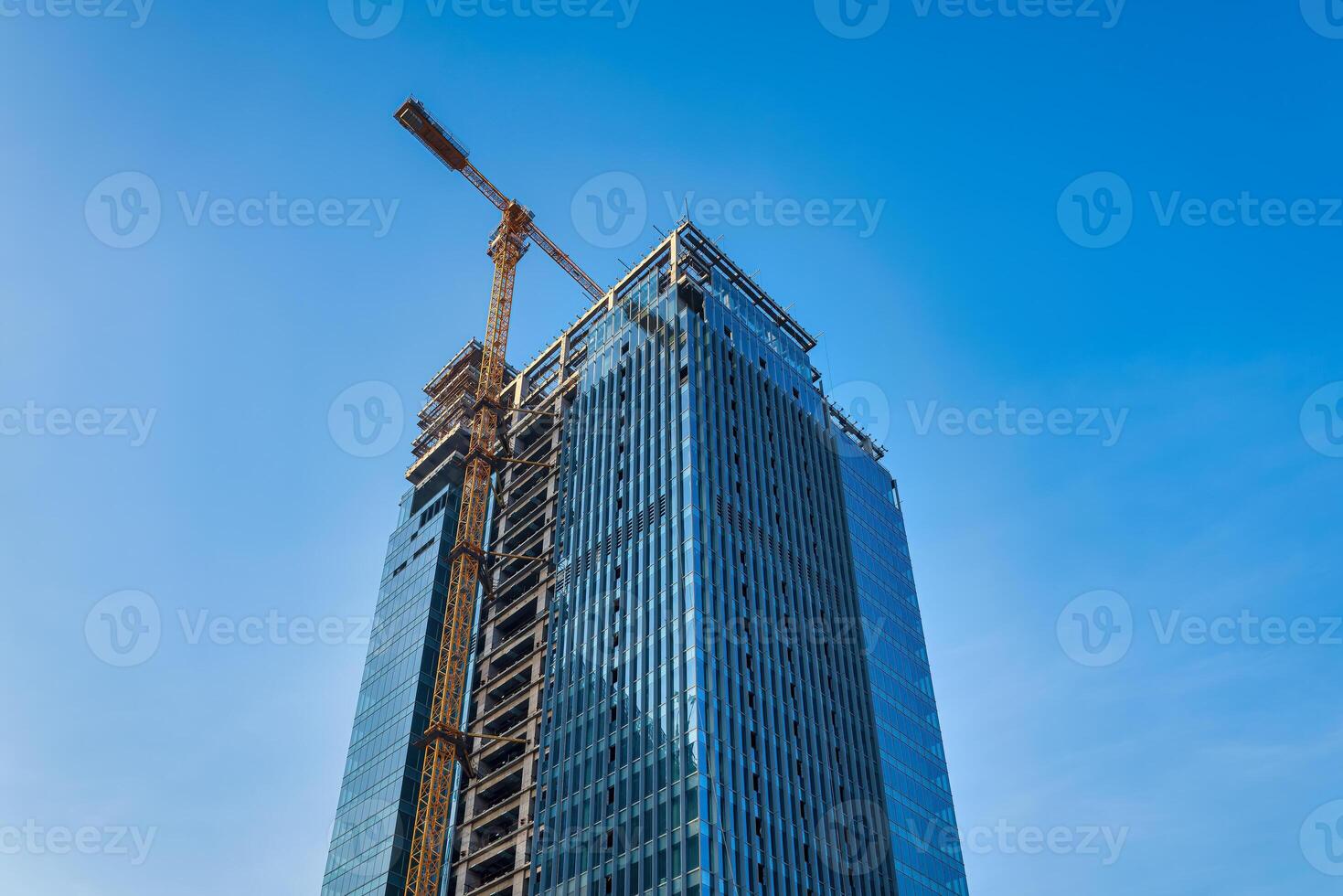 A crane building a skyscraper against a blue sky. photo