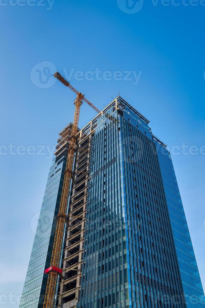 A crane building a skyscraper against a blue sky. photo