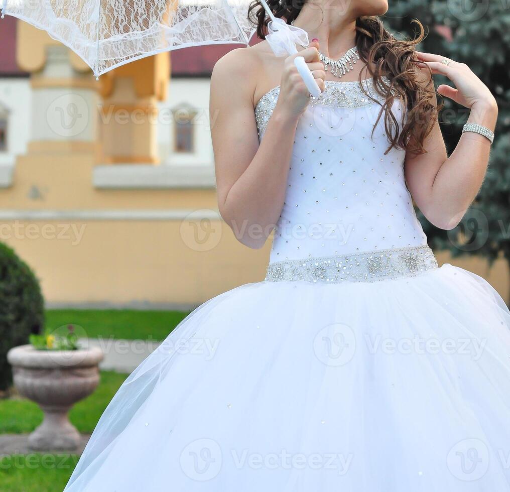 Close-up portrait of young beautiful bride in a wedding dress standing on a green field and holding a white umbrella photo