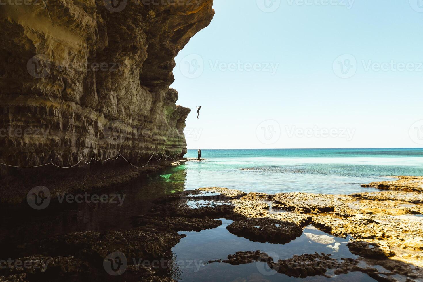 Tourist jump in water Ayia napa bay shore with crystal blue mediterranean waters and tranquil rocky stone sea caves. Sightseeing path with ropes.Texture and islands geology concept photo