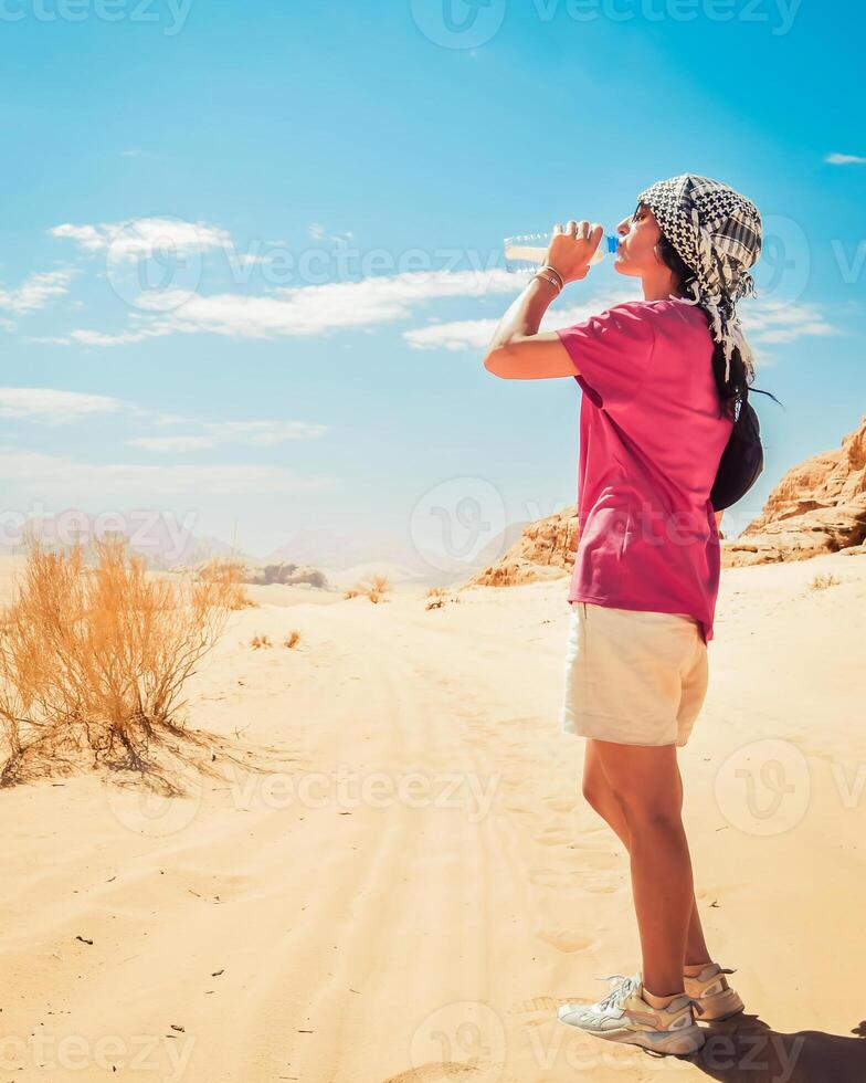 mujer caucásica sedienta bebe agua fresca fría en calor extremo en el desierto caliente de wadi rum al aire libre en la ruta de senderismo foto