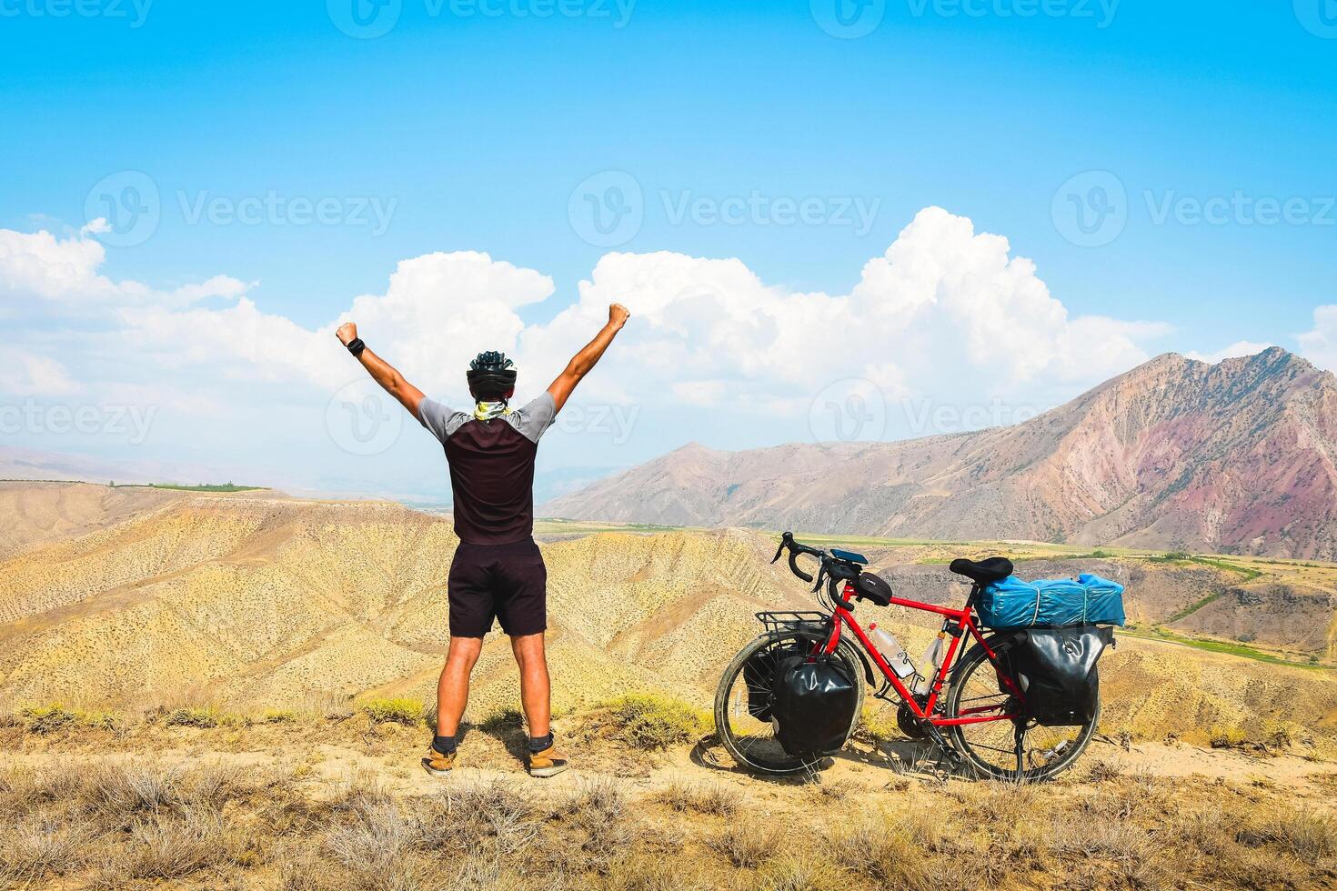 Close up back view inspirational excited joyful caucasian male cyclist on viewpoint by red touring bicycle in deserted mountains with hands up confident carefree lifestyle photo
