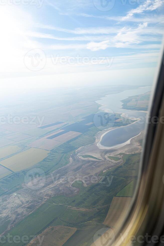Land view through the airplane window. Fields, roads, rivers from a bird's eye view. Porthole. Look out the window of a flying plane. Top view of the ground photo