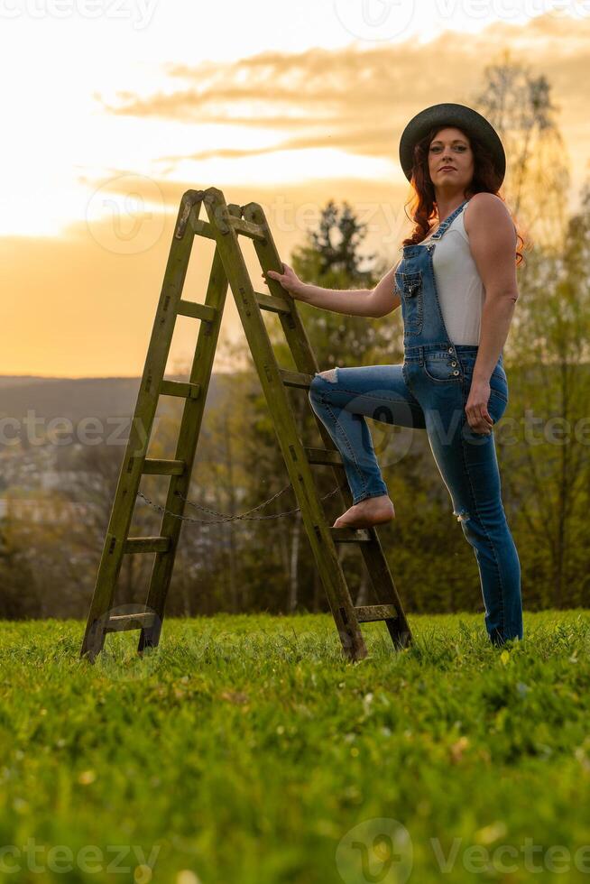 a woman in dungarees with a ladder on a meadow photo