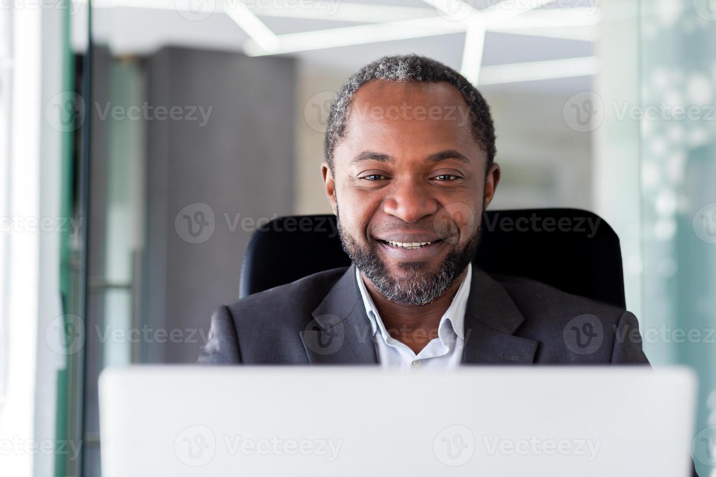 Mature adult african american businessman in middle of office working with laptop, close up man smiling looking at computer screen, satisfied with achievements boss at workplace close up. photo