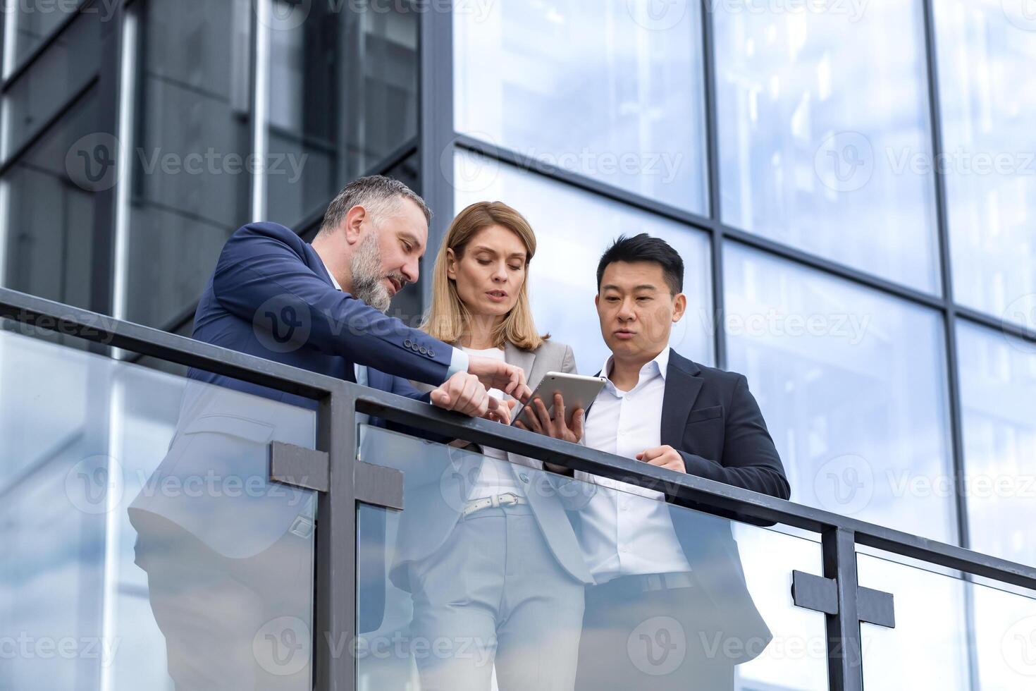 Specialist IT team leaders, group of business people outside office building, discussing and talking, testing new app on tablet, professional colleagues in business clothes, photo