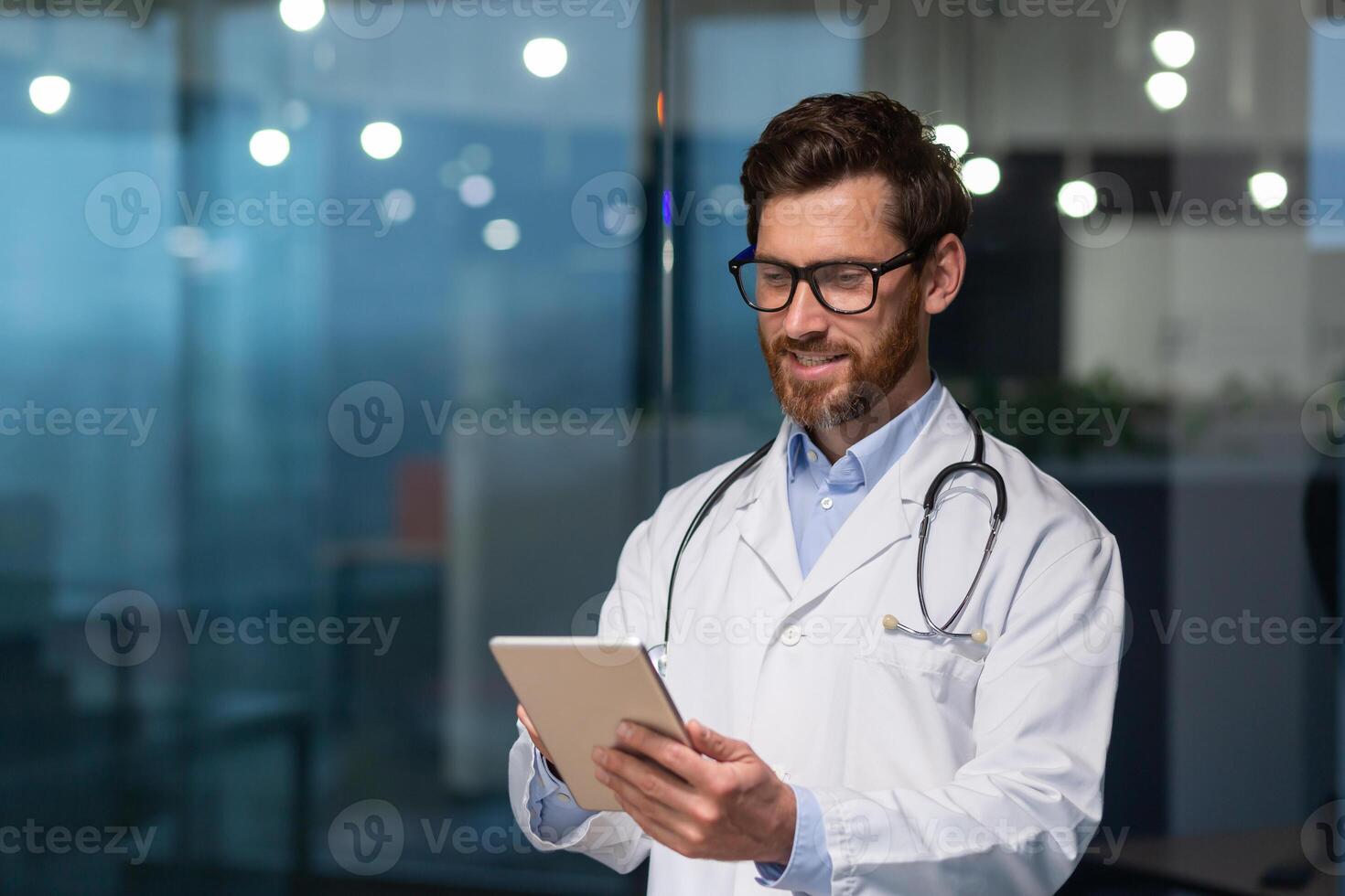 maduro y exitoso médico en médico blanco Saco y estetoscopio trabajando en aburrido clínica oficina, hombre en lentes sonriente y utilizando tableta computadora, para en línea paciente consulta. foto