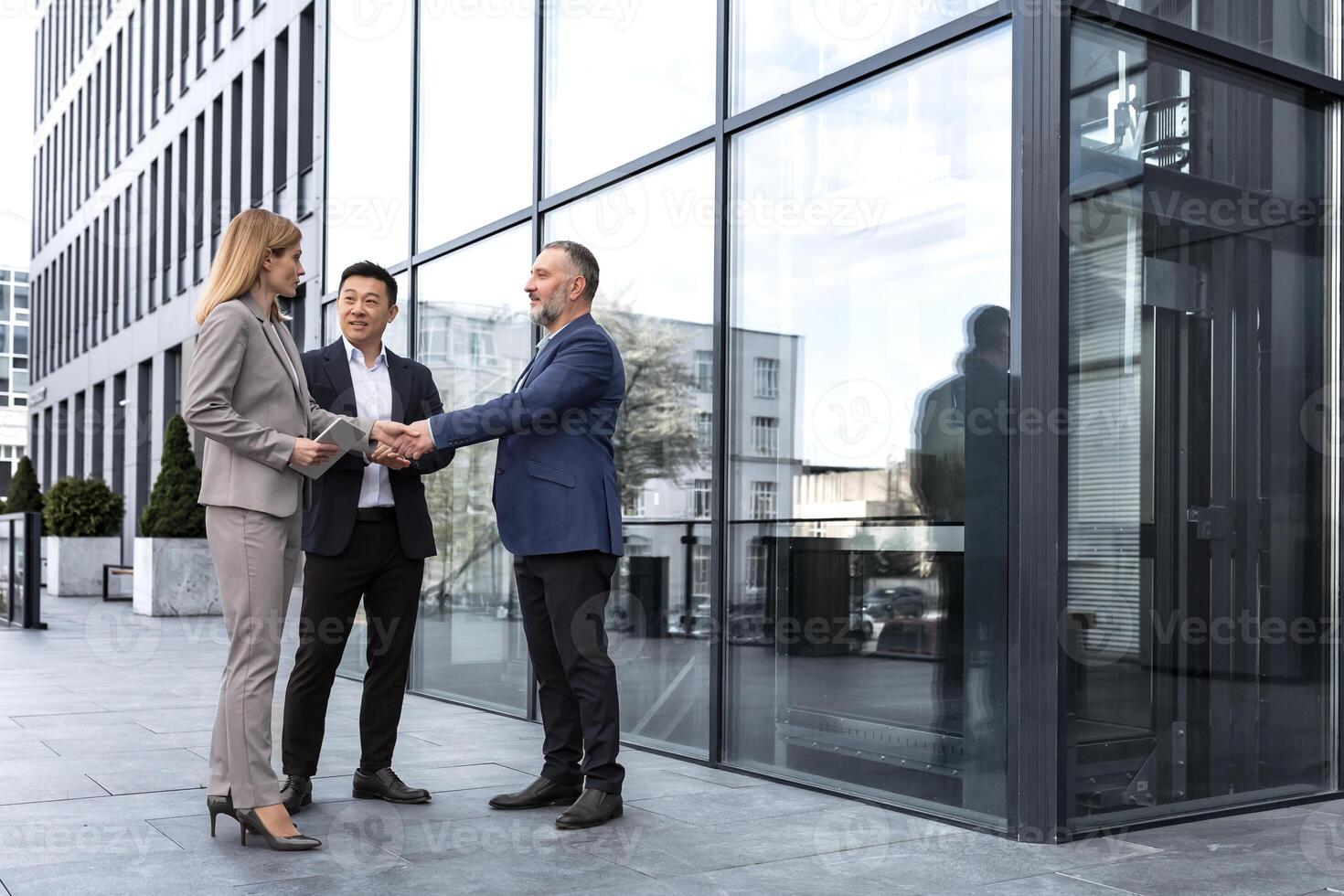 Meeting of three colleagues from outside the office building, experienced and mature IT specialists, greeting and shaking hands, business persons in business suits, diverse group of people photo