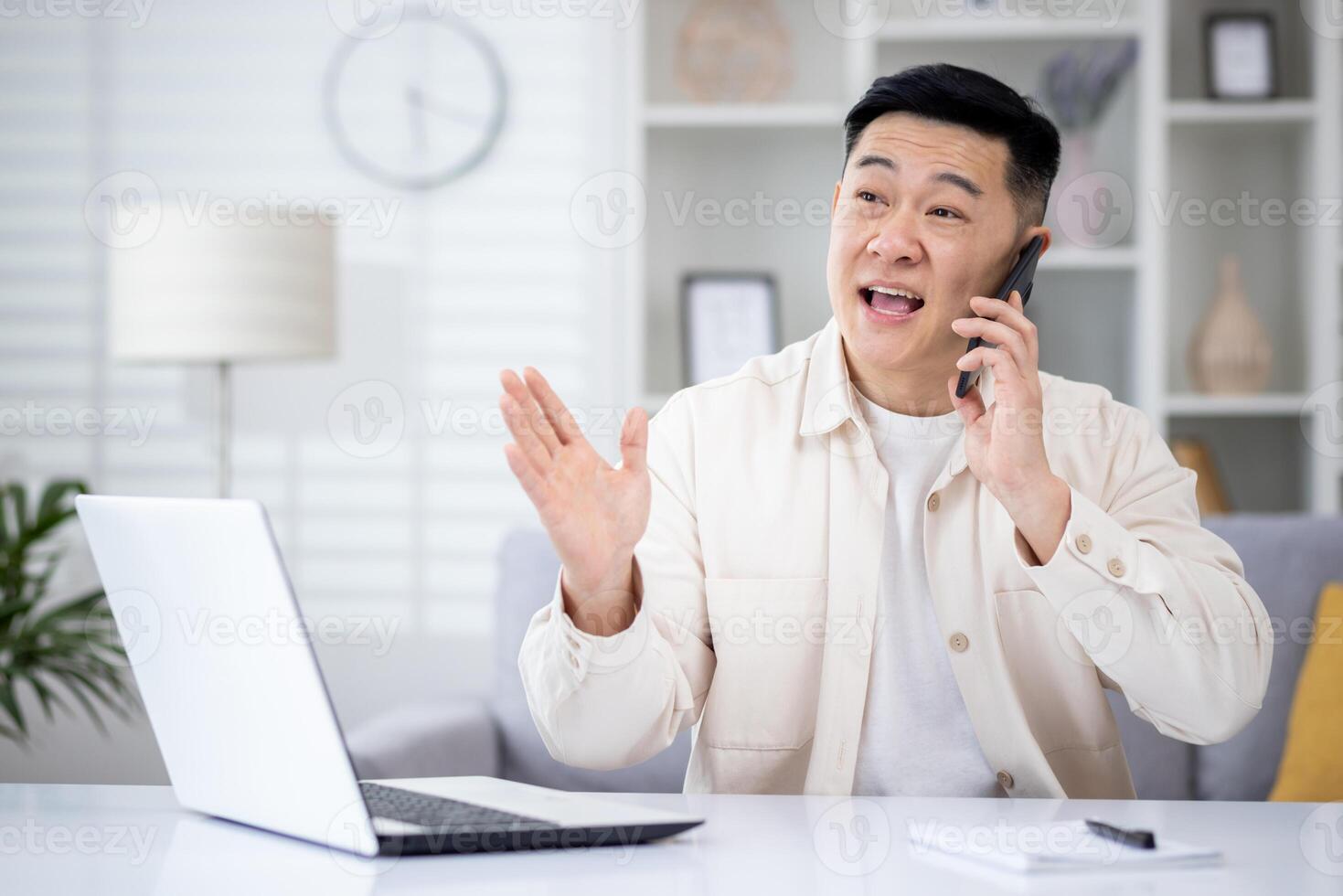 Mature asian man talking on the phone at home, man working in home office sitting at desk in home office, happy and smiling, consulting clients remotely. photo