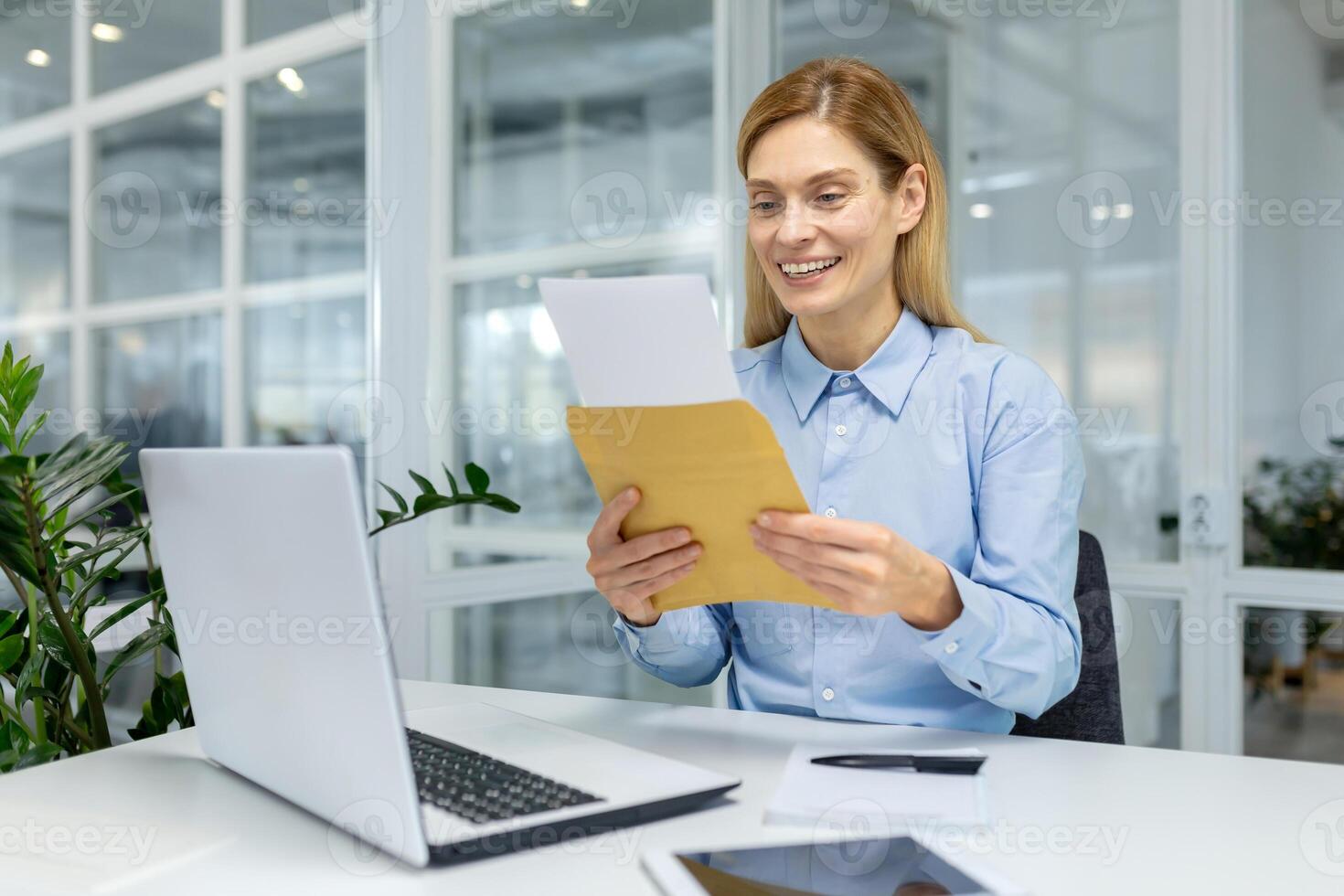 Smiling professional woman reading a letter, expressing joy and satisfaction at her office workspace. photo