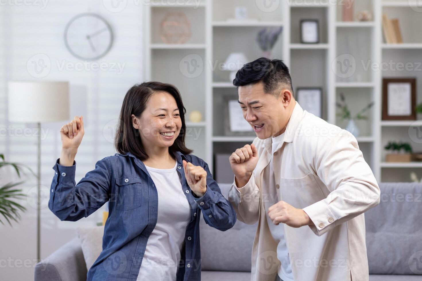 contento asiático Pareja hombre y mujer bailando juntos a hogar en tiempo de día en vivo habitación, contento joven familia celebrando contento día y Boda aniversario. foto